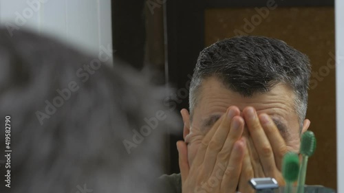 Close-up of tired after working day man washes his face in front of the mirror with water photo