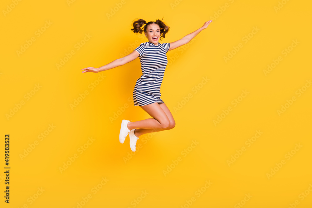 Photo of sweet funny young woman wear striped clothes jumping arms sides isolated yellow color background