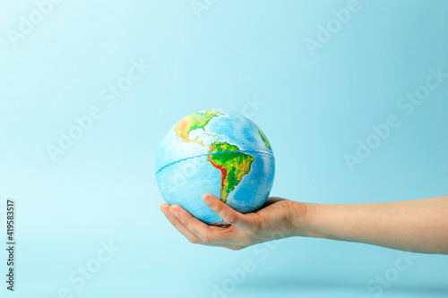 Earth globe in hands on a clean blue background. The concept of protecting nature, ecology and global peace
