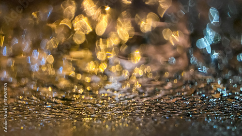 Yellow bokeh effect in night or evening street lighting on car glass in frost. Winter abstract background. A drop of water on the window. The lights are out of focus