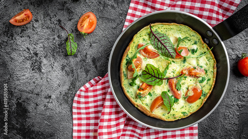 Frying pan with cheese, tomatoes, spinach frittata on dark background. Keto, ketogenic breakfast, lunch. Long banner format, top view