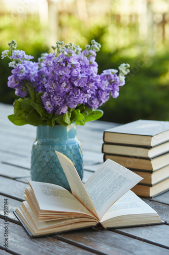 A pile of books and a vase with flowers on a wooden table
