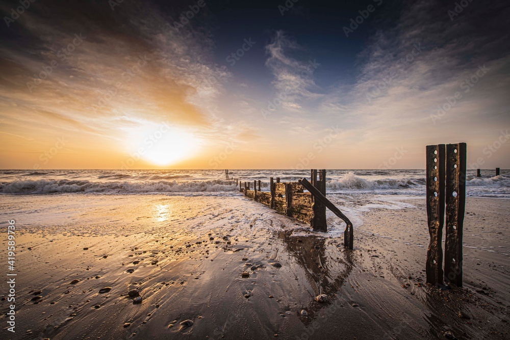 Sunrise at The Warren, Folkestone. A winter sunrise lights the sky behind the old sea groynes on The Warren at low tide. These groynes are only visible when the tide is out. They show evidence of the 
