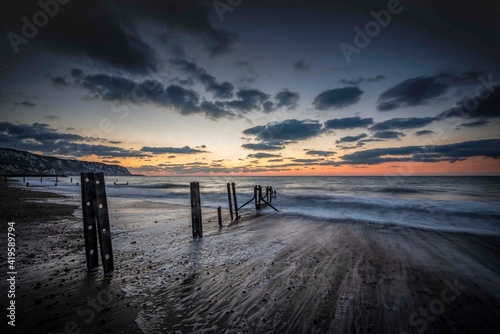 Sunrise at The Warren, Folkestone. A winter sunrise lights the sky behind the old sea groynes on The Warren at low tide. These groynes are only visible when the tide is out. They show evidence of the 
