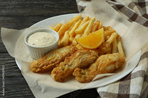 Plate with fried fish and chips on wooden background with kitchen towel