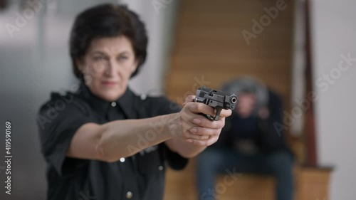 Female hands raising holding armed gun with blurred policewoman and desperate burglar or murderer at background. Confident Caucasian police officer catching criminal indoors.