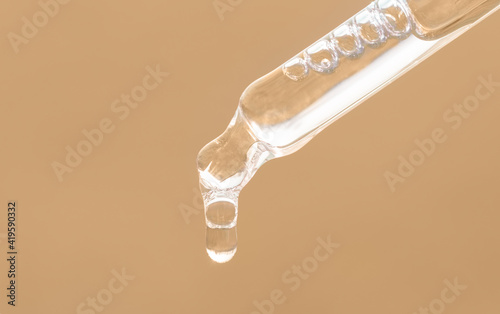 Pipette with essential oil, serum with peptides, emulsion, hyaluronic acid on beige background. Closeup of beige dropper, falling drop of oil close up. Beauty skincare product. Self care concept