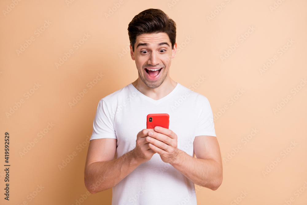 Portrait of astonished funny guy open mouth staring phone unexpected comment isolated on beige color background Portrait of astonished funny guy open mouth staring phone unexpected comment isolated on beige color background