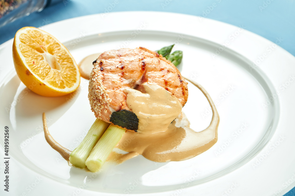 Appetizing salmon steak with asparagus and sauce in a white plate on a blue tablecloth. Appetizing salmon steak with asparagus and sauce in a white plate on a blue tablecloth.