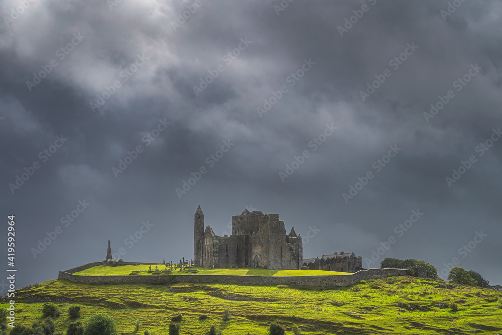 Rock of Cashel castle illuminated by sunlight and surrounded by dramatic dark storm clouds. Known as Cashel of Kings or St. Patricks Rock, Ireland