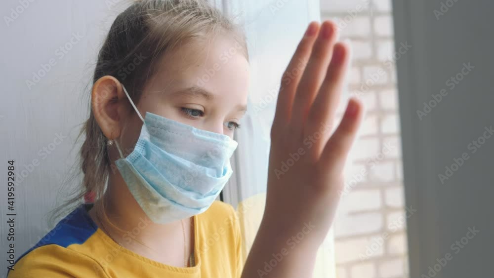 Little girl in a protective mask sits in quarantine at home. Stay at home, stay safe. Protection against virus and infection. Concept of coronavirus quarantine or covid-19. Little girl in a protective mask sits in quarantine at home. Stay at home, stay safe. Protection against virus and infection. Concept of coronavirus quarantine or covid-19.