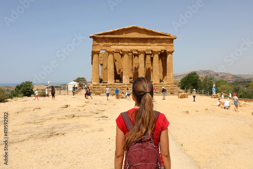 Female tourist with backpack visiting Concordia temple in the Valley of temples near Agrigento in Sicily, Italy