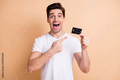 Photo of astonished guy open mouth direct finger debit card unexpected promo isolated on beige color background