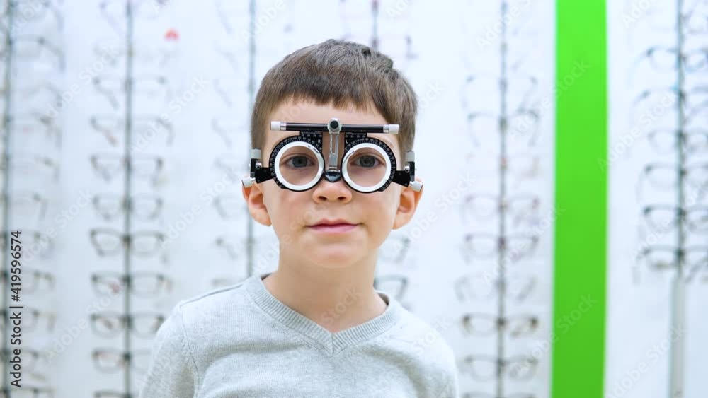 The boy stands on a background of a show-window with frames for spectacles with the device for selection of contact lenses The boy stands on a background of a show-window with frames for spectacles with the device for selection of contact lenses