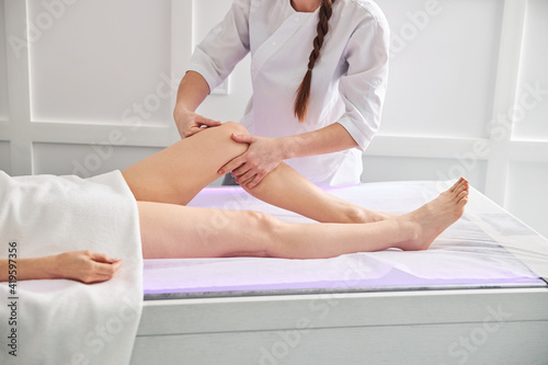 Professional masseuse massaging woman leg in spa salon
