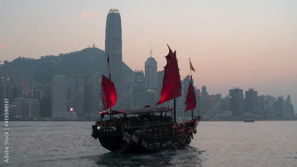 A wooden red-sailed junk boat is seen sailing at Victoria Harbour waterfront and in front of the Hong Kong Island skyline as it has become an iconic touristic attraction in Hong Kong.