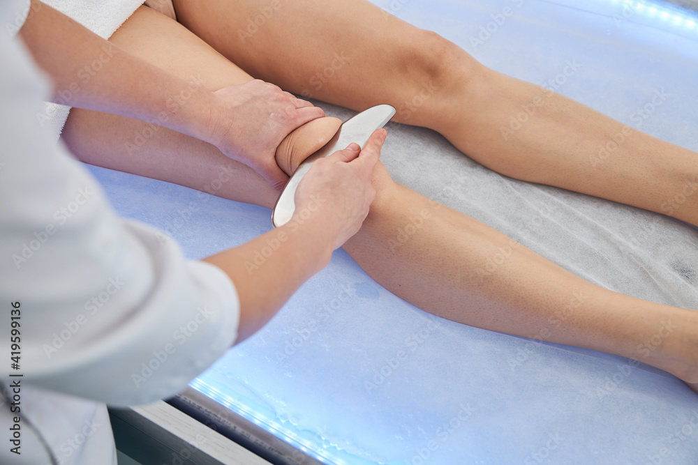 Fototapeta premium Physical therapist massaging woman leg with metal tool