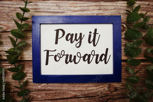 Pay it Forward written on blue frame with green leave flat lay on wooden background
