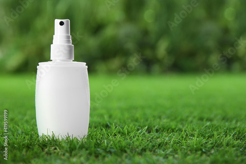 Bottle of insect repellent spray on green grass. Space for text