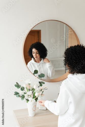 Woman with African curls in a white sweater touches a bouquet of flowers with her hand