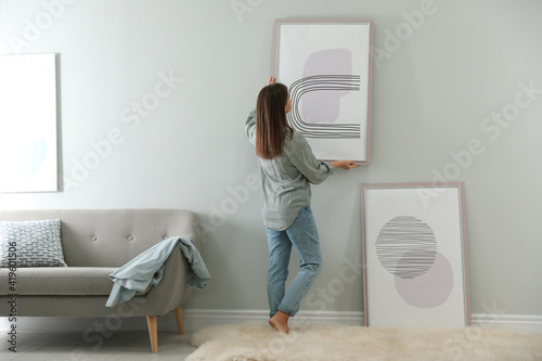 Obraz na plátně Woman hanging picture on wall in room. Interior design