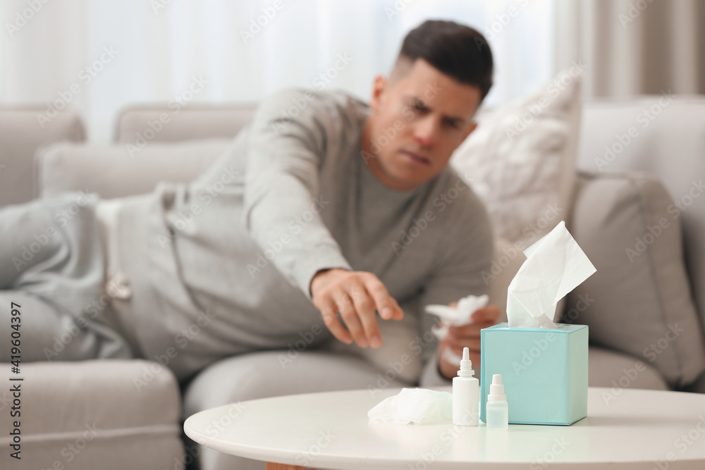 Ill man at home, focus on nasal spray, drops and box of tissues Ill man at home, focus on nasal spray, drops and box of tissues