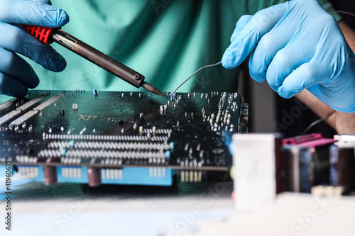 Technician repairing electronic circuit board with soldering iron at table, closeup