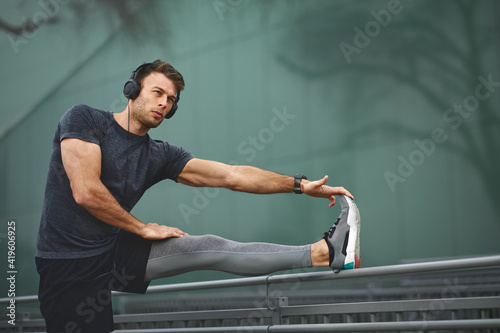 Fotografia Young man in sports clothes and headphones on his head stretching  legs before t