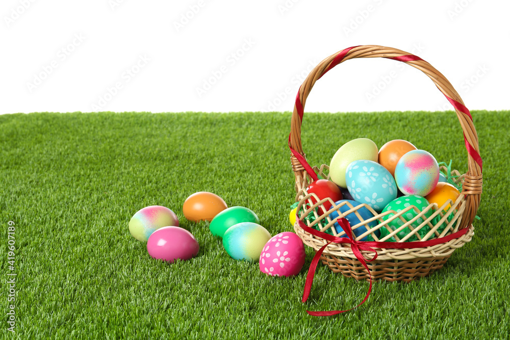 Wicker basket with Easter eggs on green grass against white background. Space for text Wicker basket with Easter eggs on green grass against white background. Space for text