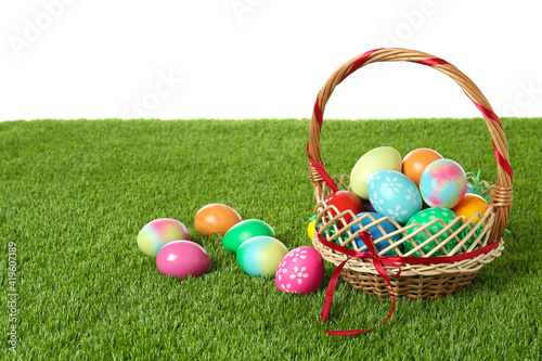 Wicker basket with Easter eggs on green grass against white background. Space for text