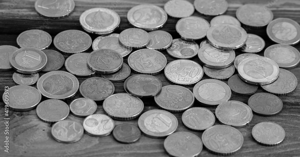 Euro coins on a wooden table. Money, finance, and economics. Black and white image. Selective focus. Euro coins on a wooden table. Money, finance, and economics. Black and white image. Selective focus.