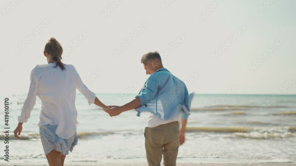 joyful lovely Couple Having Fun walking Along sandy Beach Together. beautiful young woman in white shirt and blue skirt and handsome adult man in casual shirt and jeans enjoying at seaside joyful lovely Couple Having Fun walking Along sandy Beach Together. beautiful young woman in white shirt and blue skirt and handsome adult man in casual shirt and jeans enjoying at seaside
