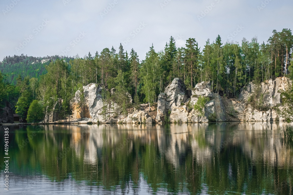 The green forest is reflected in the water. Rock on the lake shore. Summer landscape