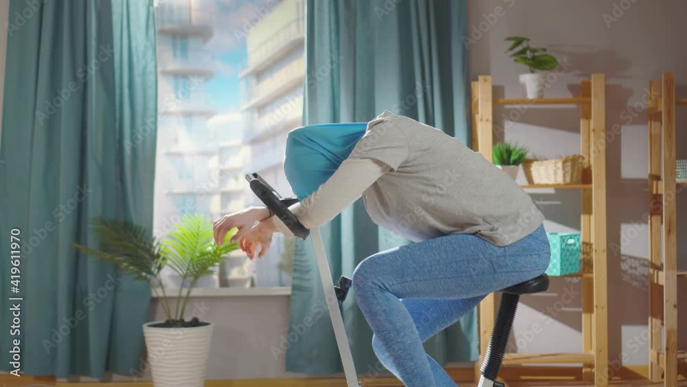 Tired muslim woman in a national headscarf is working out on an exercise bike in her living room Tired muslim woman in a national headscarf is working out on an exercise bike in her living room