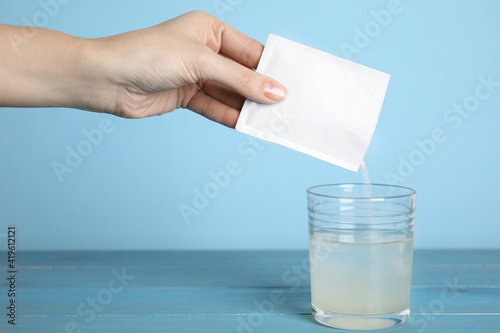 Fotografija Woman pouring powder from medicine sachet into glass of water on blue wooden tab
