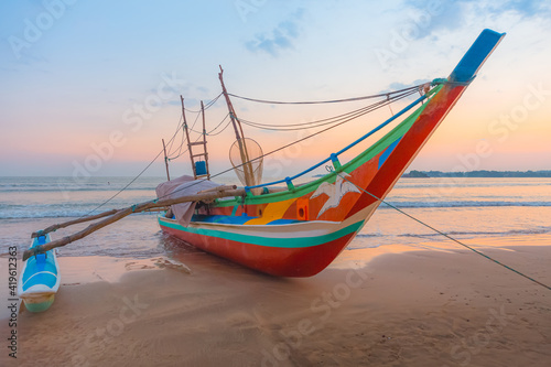 Fototapet A traditional Sri Lankan fishing catamaran boat during a colourful sunrise or sunset on Weligama, Beach in Sri Lanka