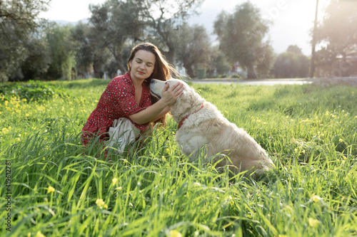 Beautiful woman playing with her golden retriever dog in green grass field. Outdoor portrait. Sunset light. Summer or spring