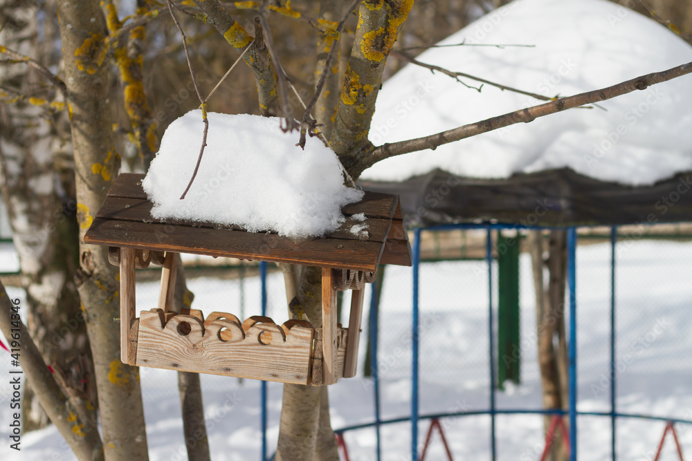 Wooden bird feeder hanging in the park on a tree in the snowy winter Wooden bird feeder hanging in the park on a tree in the snowy winter