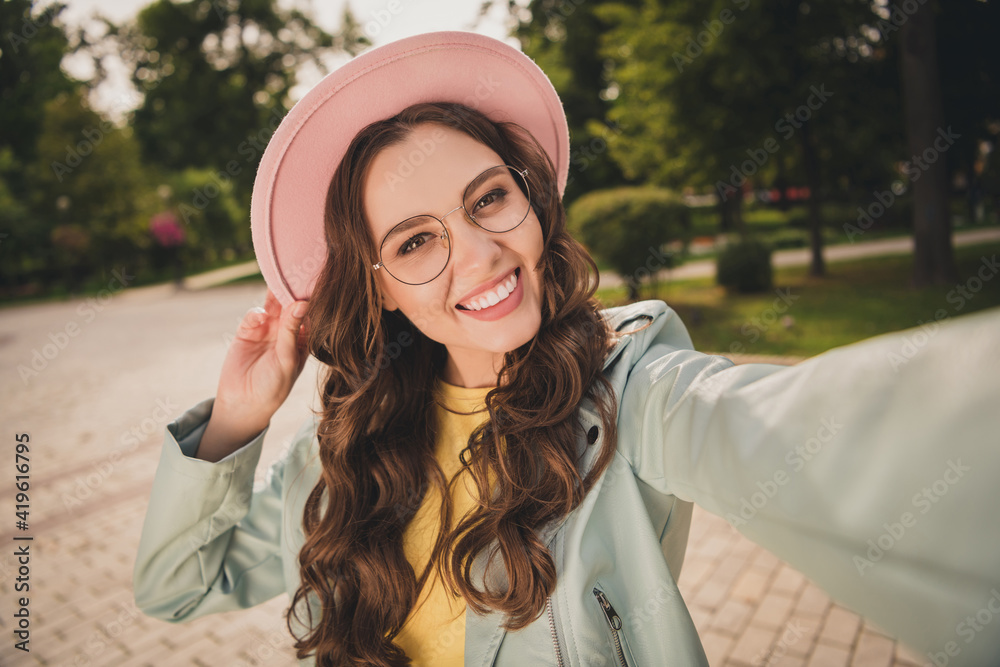 Photo of shiny young woman dressed teal jacket glasses bag arm cap walking tacking selfie outdoors city park