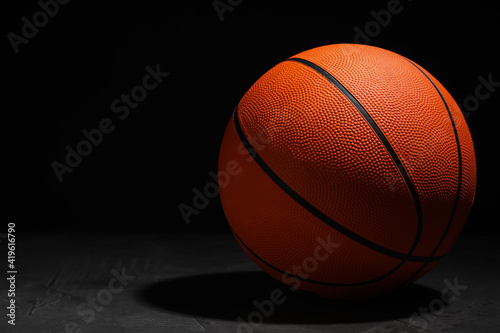 Basketball ball on grey stone table against dark background, space for text © New Africa