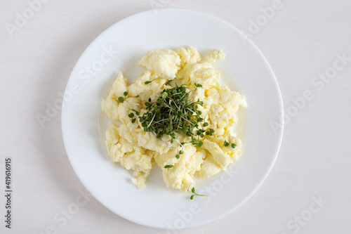 Scrambled eggs with microgreens on a white plate. Close up.