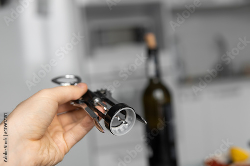 Metal corkscrew in a man's hand with a bottle of red wine on a background with a light white kitchen. Wine lover. Wine opener.