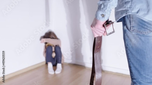 Scared little girl looking at man with belt, corporal punishment, bad parenting