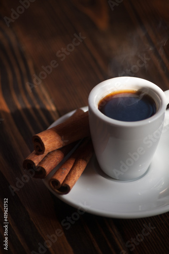 A cup of aromatic black coffee. Morning espresso or Americano coffee for breakfast in a beautiful cup. Cinnamon sticks. Wooden background. 