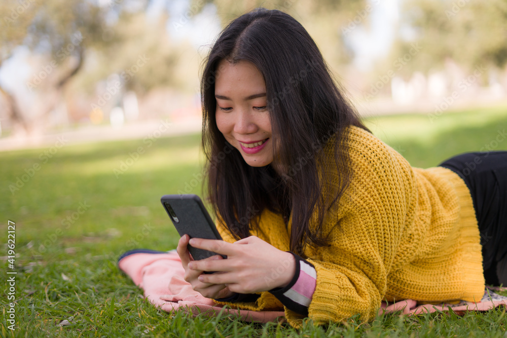 relaxed Asian woman using mobile phone in city park - lifestyle portrait of young happy and pretty Chinese girl lying on green grass networking on smart phone relaxed Asian woman using mobile phone in city park - lifestyle portrait of young happy and pretty Chinese girl lying on green grass networking on smart phone