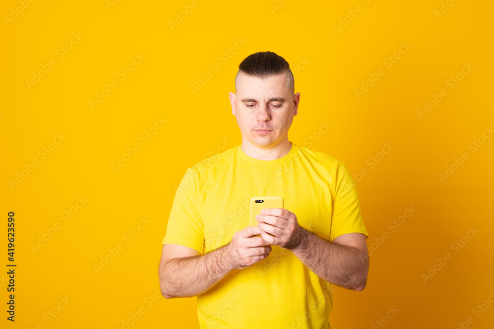 Young man texting message on smartphone on yellow background. Smiling man holding smartphone and looking at it. Happy man writing a message on the phone. Young man texting message on smartphone on yellow background. Smiling man holding smartphone and looking at it. Happy man writing a message on the phone.