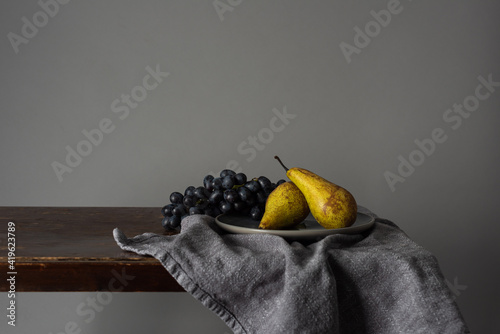Stilleben / Still life with fruits. Grapes and pears on a rustic table indoors with a moody window light
