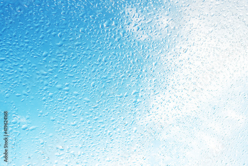 Rain drops on surface of the window glass with sky cloud background. Natural pattern of water drops on glass