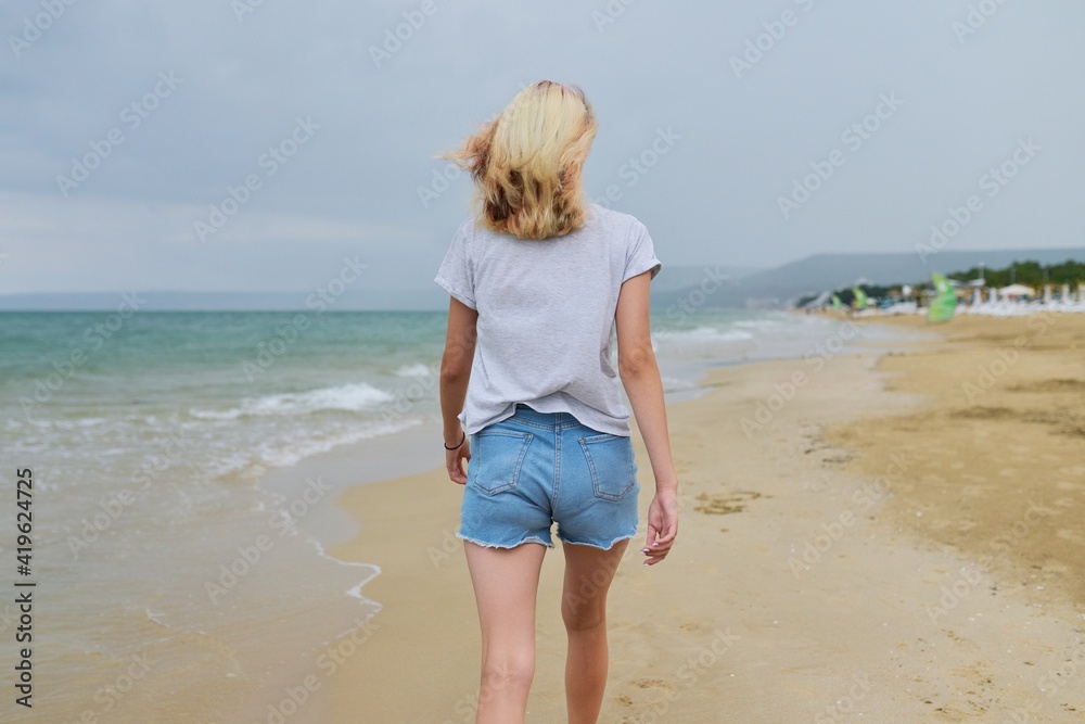 Young beautiful woman walking along evening beach, back view Young beautiful woman walking along evening beach, back view