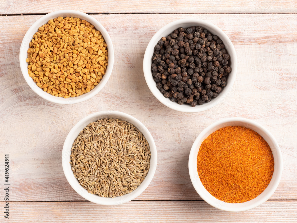 Spice red and black pepper, cumin, fenugreek in a white bowl on a light wooden background Spice red and black pepper, cumin, fenugreek in a white bowl on a light wooden background